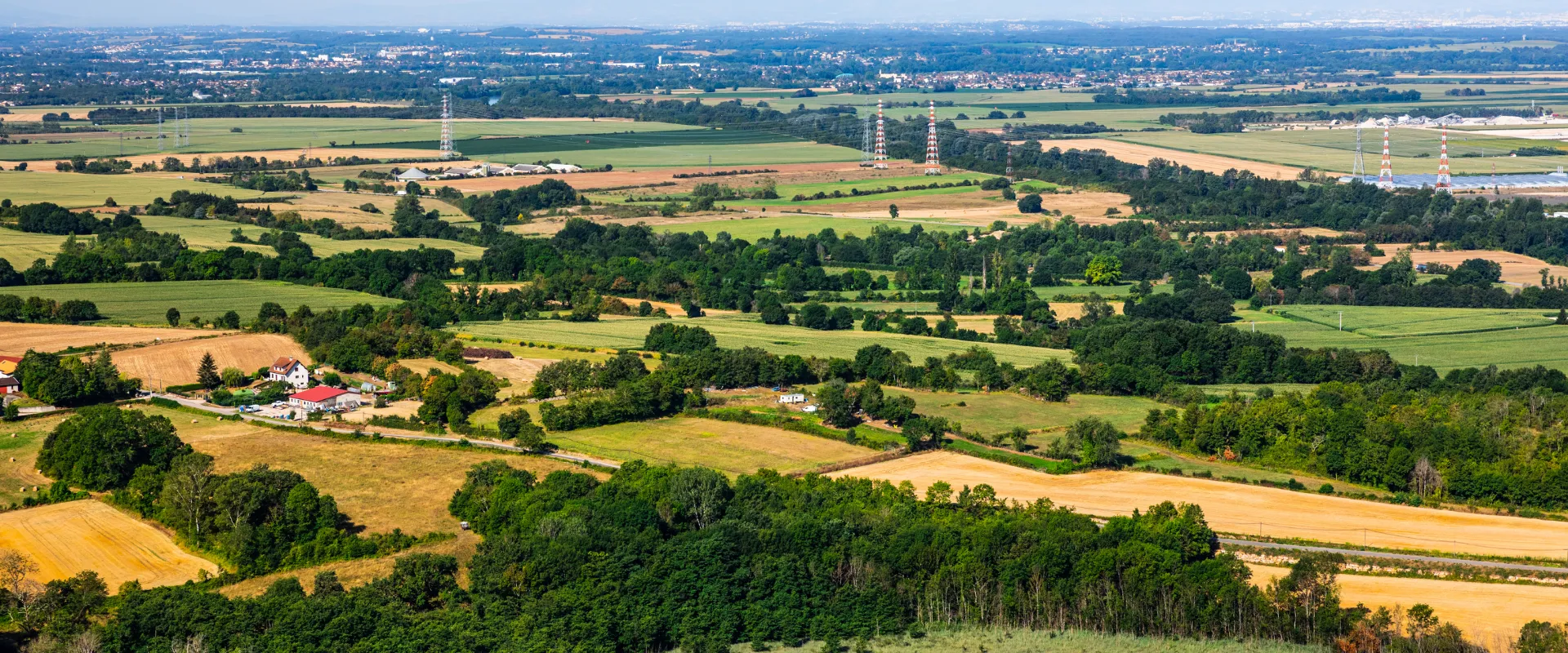 Paysage rural du département de l'Ain avec champs agricoles, forêts et pylônes électriques.