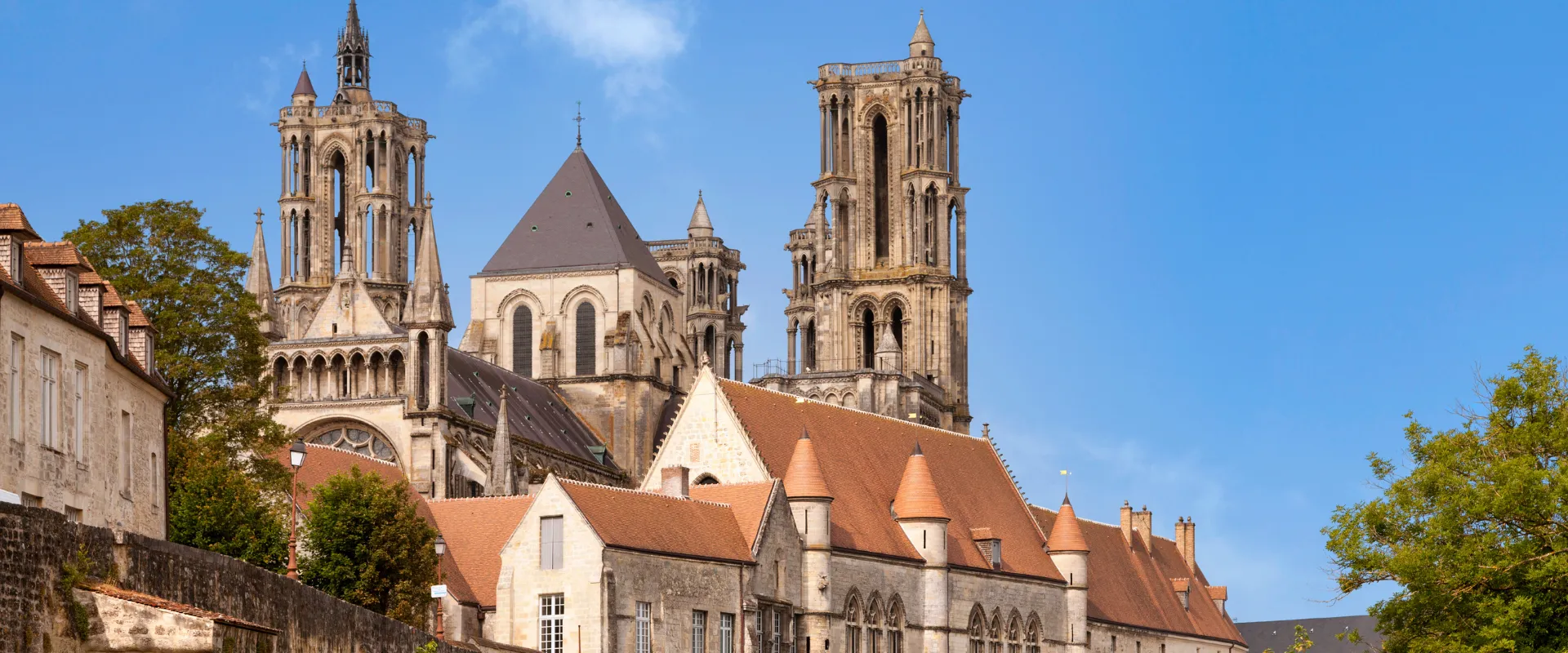 Cathédrale gothique avec tours élancées et bâtiments médiévaux en pierre beige.