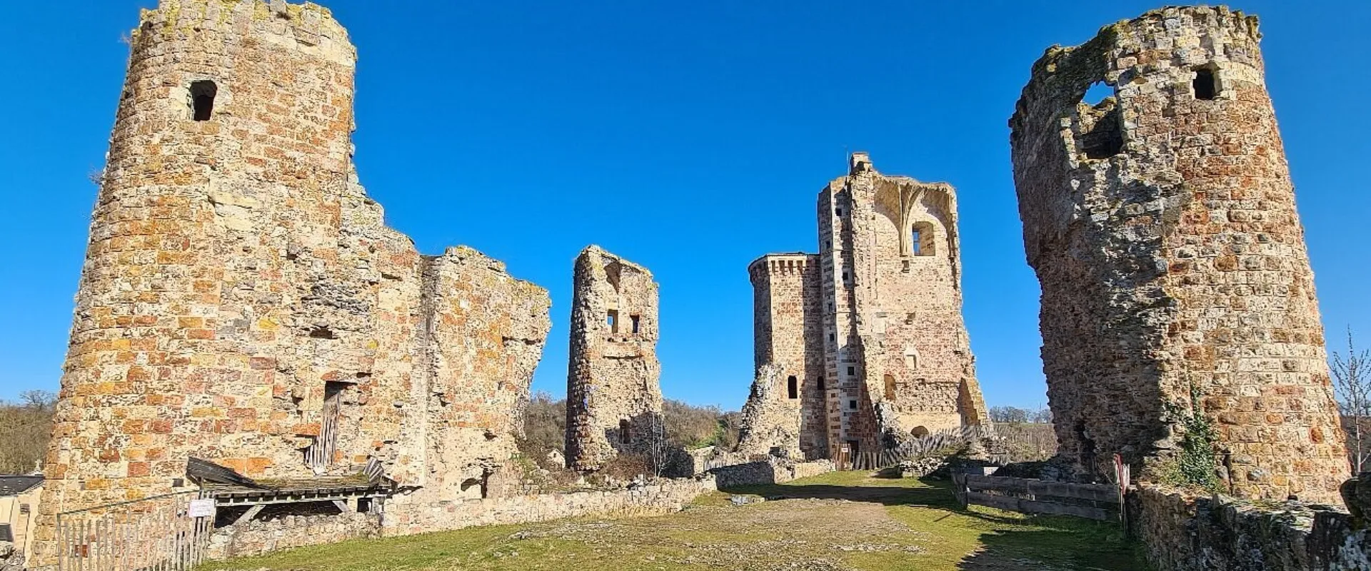 Ruines médiévales du château de Bourbon-l'Archambault avec tours en pierre et ciel bleu clair.