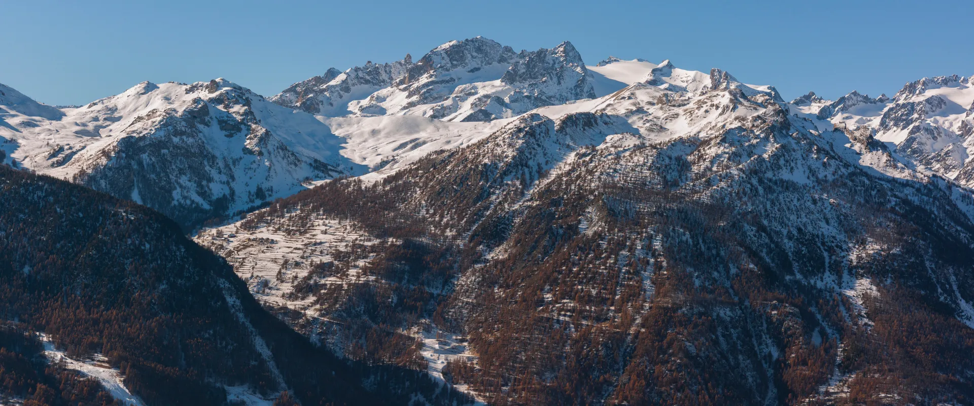Paysage montagneux enneigé des Hautes-Alpes avec forêts de mélèzes et sommets alpins.