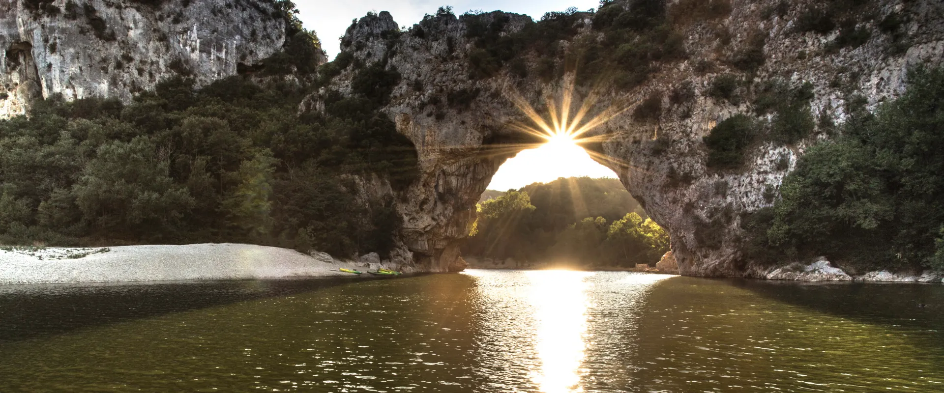 Pont d'Arc natural stone arch spanning river with sunlight in Ardèche gorge France