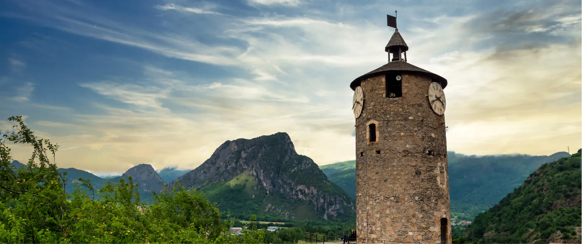 Tour de guet en pierre avec horloges dans vallée montagneuse pyrénéenne verdoyante Ariège.