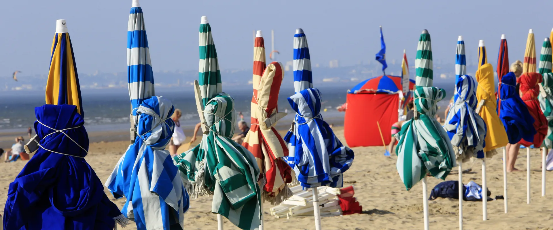 Rangée de cabines de plage colorées rayées bleu blanc rouge vert jaune sur sable Calvados.
