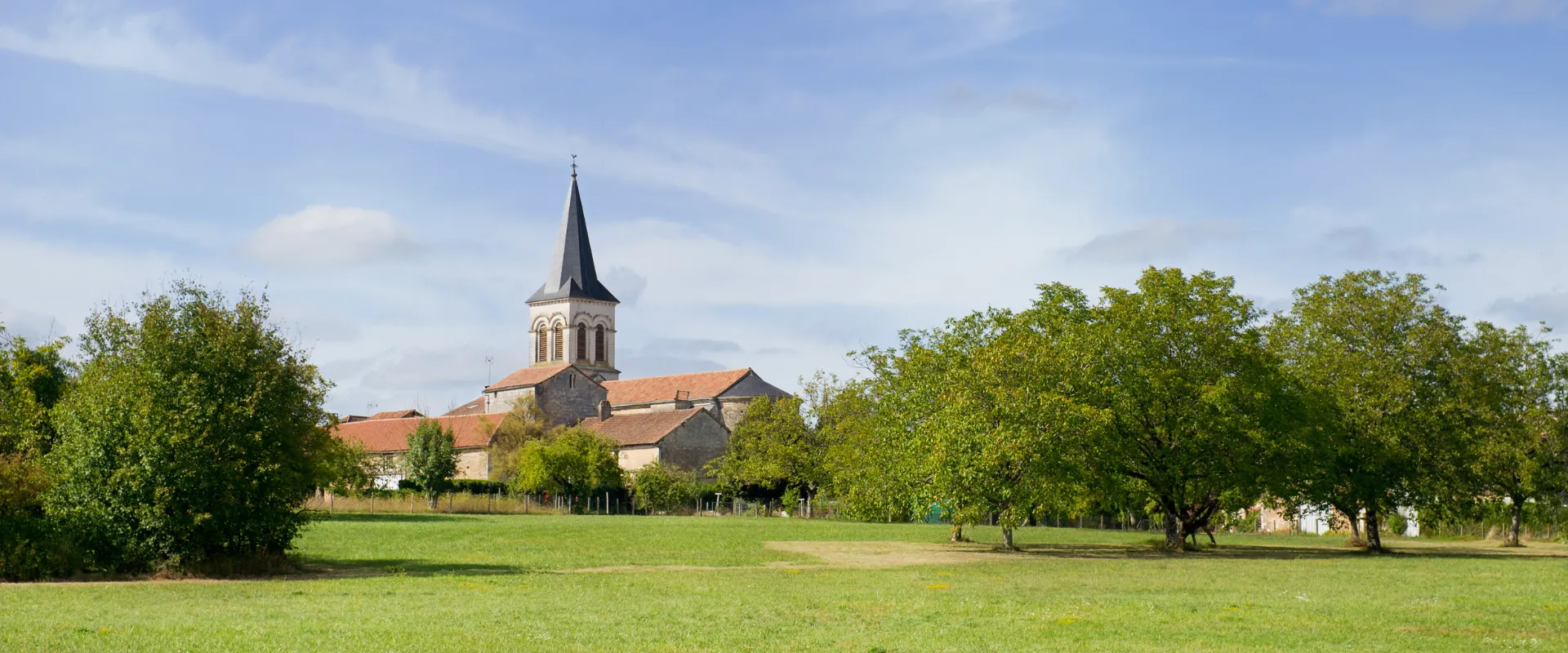 Église avec clocher pointu entourée de verdure et arbres en Charente.