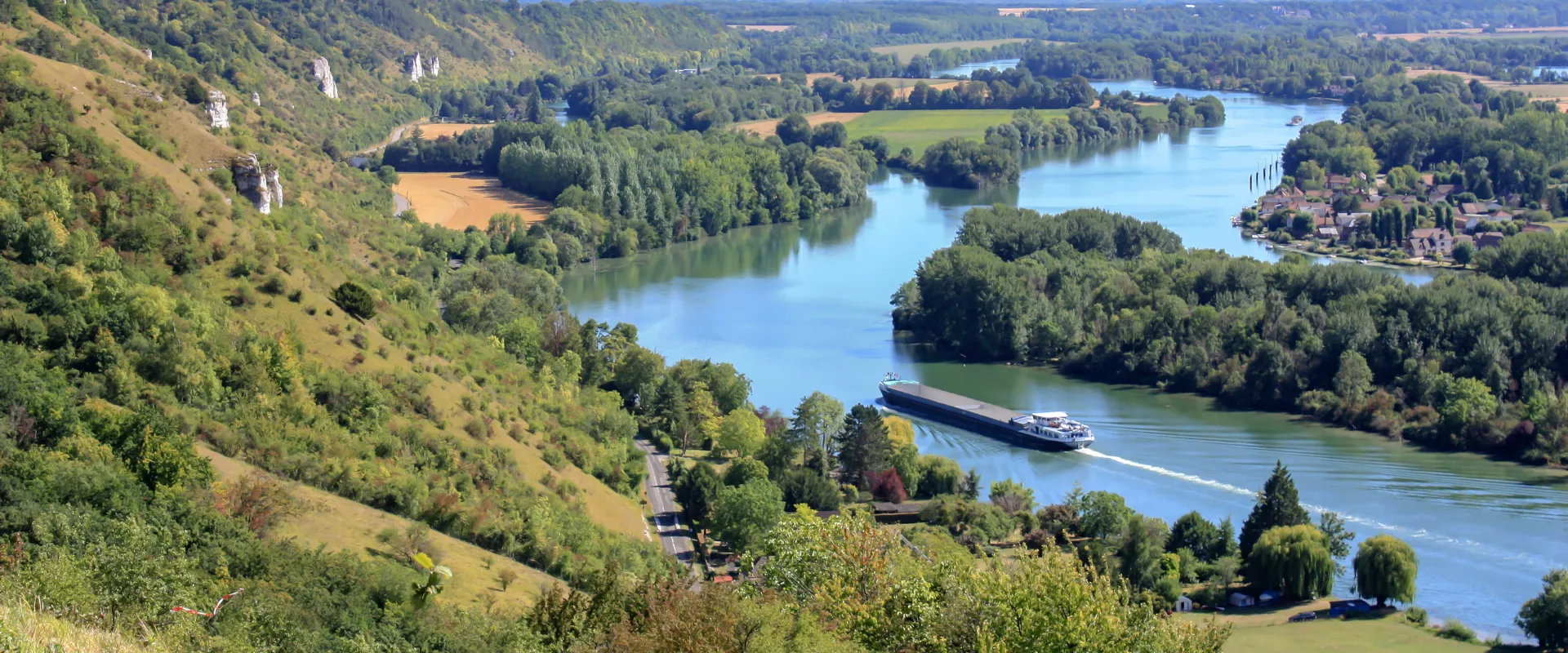 Vallée de la Seine avec bateau fluvial, falaises blanches et villages riverains en Normandie.