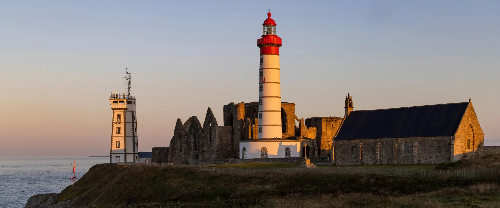 Phare rayé rouge et blanc avec chapelle en pierre au coucher du soleil, Finistère Bretagne.