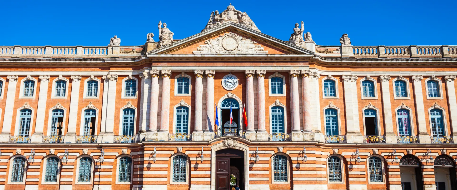 Capitole de Toulouse bâtiment en brique rouge avec colonnes blanches et ciel bleu.