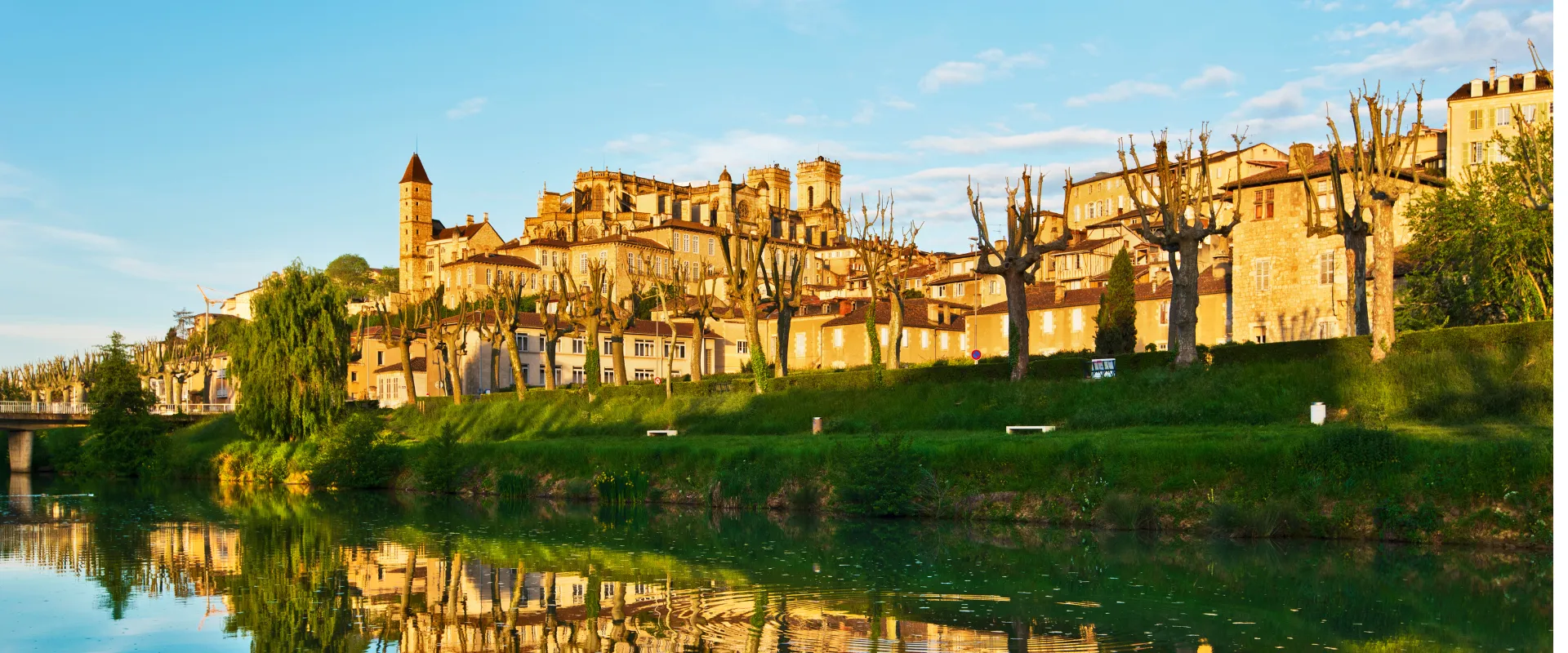 Ville médiévale jaune dorée avec château et église reflétés dans rivière verte.