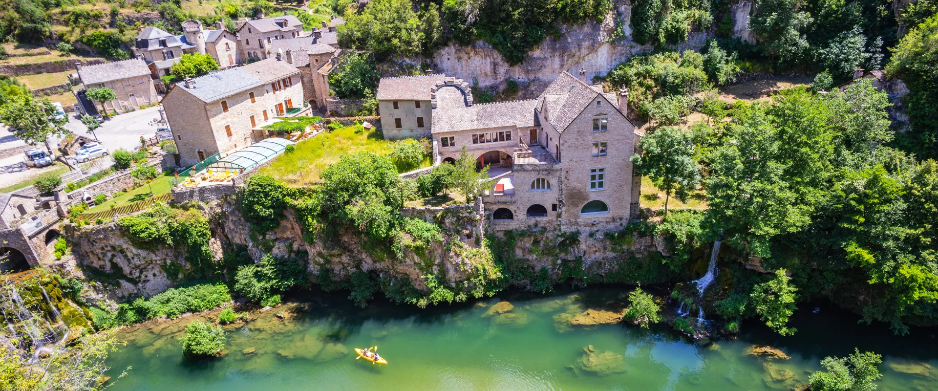 Village médiéval en pierre au bord d'une rivière turquoise entouré de végétation luxuriante.