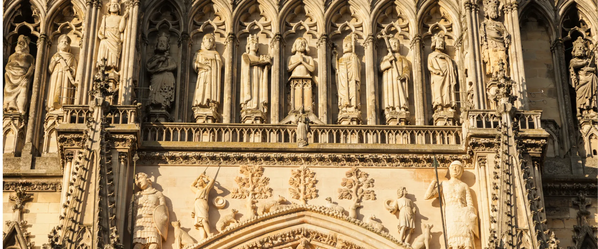 Façade gothique de cathédrale avec statues de saints et ornements architecturaux sculptés en pierre.