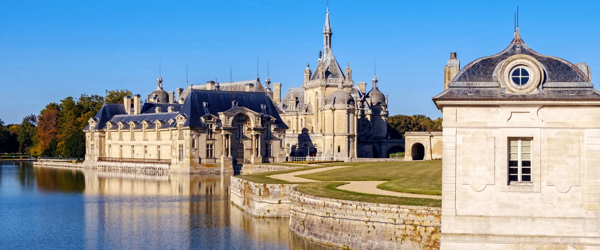 Château de Chantilly avec ses tours pointues reflétées dans l'eau calme.