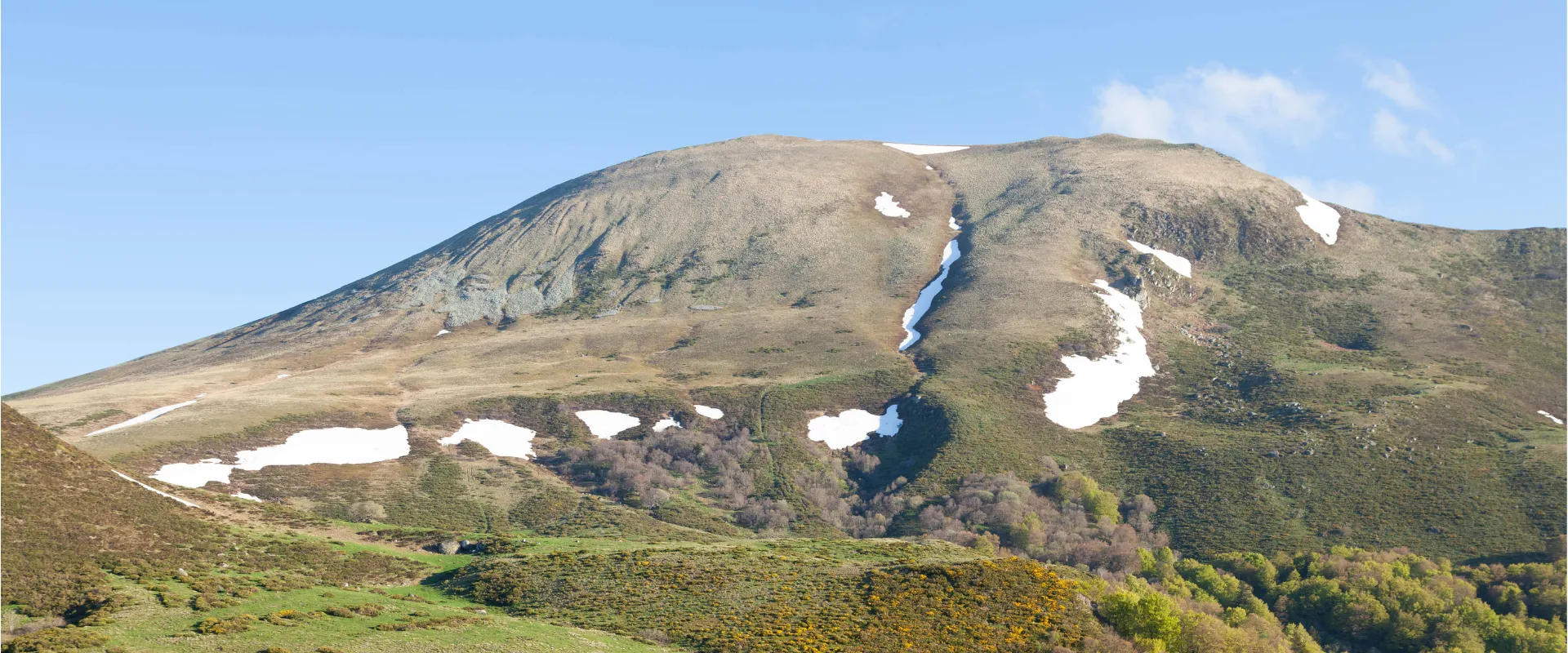 Volcan du Puy-de-Dôme avec neige résiduelle, forêt et ruisseau au printemps.