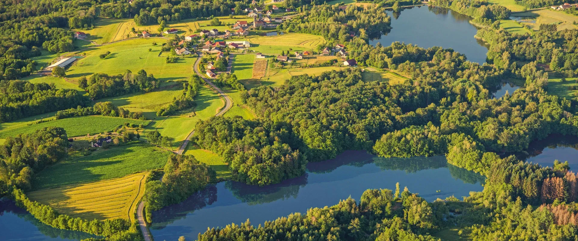 Village rural avec lacs, forêts et champs agricoles verts, Rhône.