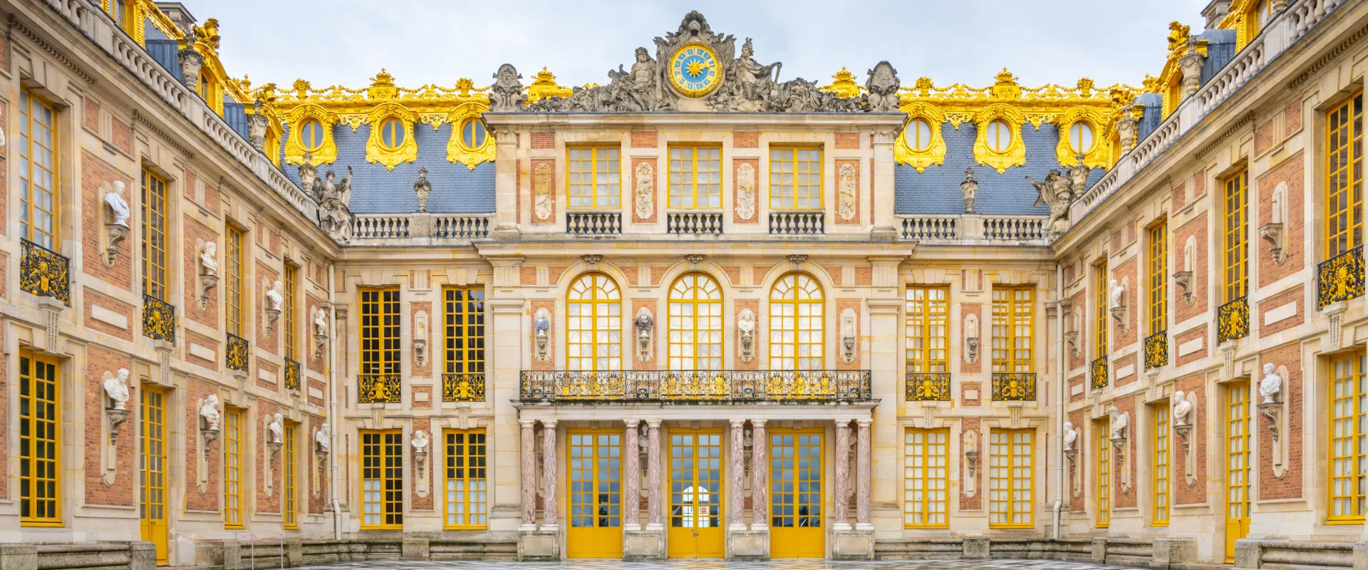 Cour intérieure du Château de Versailles avec façade dorée et portes jaunes majestueuses.