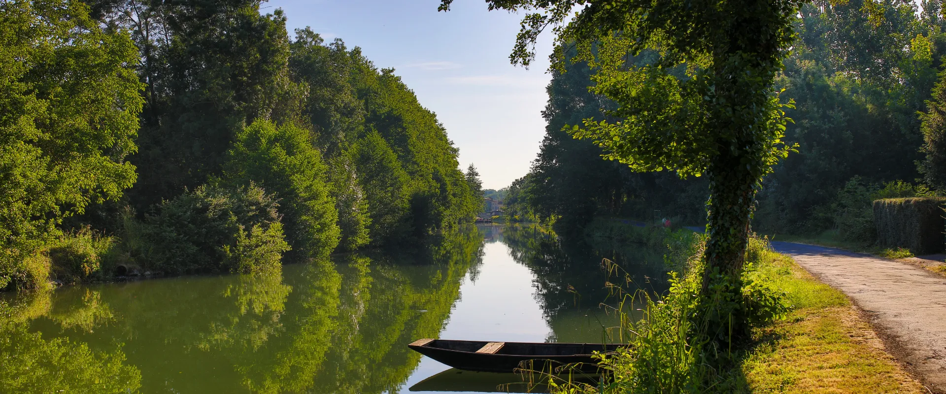 Barque noire sur canal bordé d'arbres verts luxuriants en Deux-Sèvres