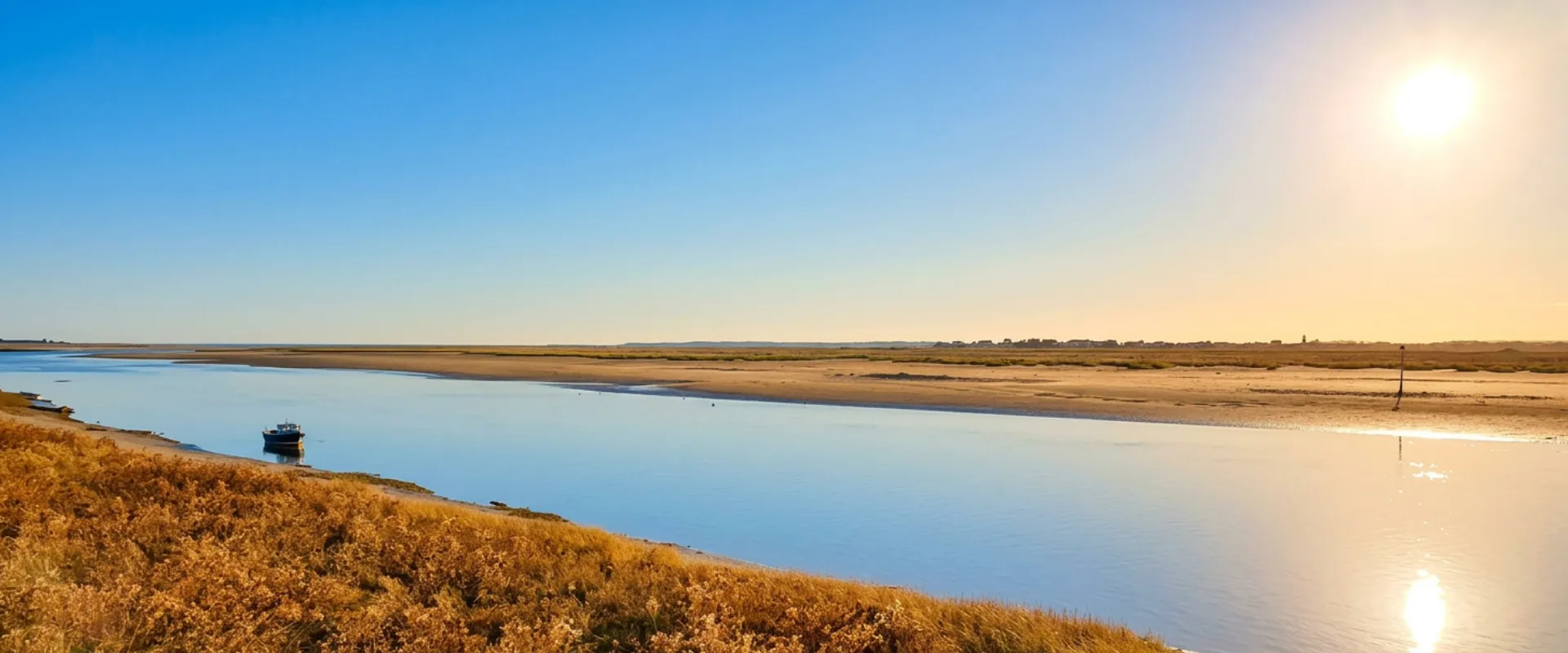 Baie de Somme avec bateau, marais salants et ciel bleu dégagé.