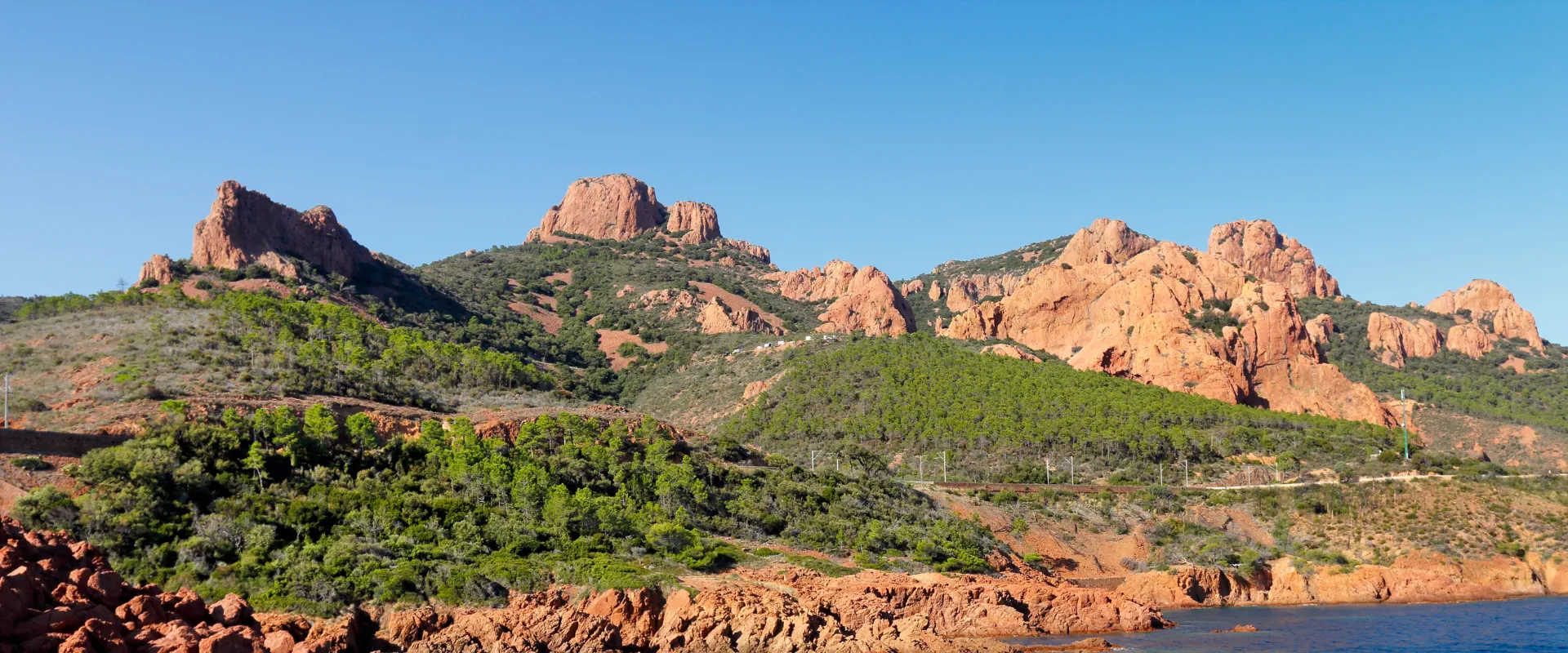 Paysage côtier du Var avec roches rouges, végétation méditerranéenne et mer bleue.