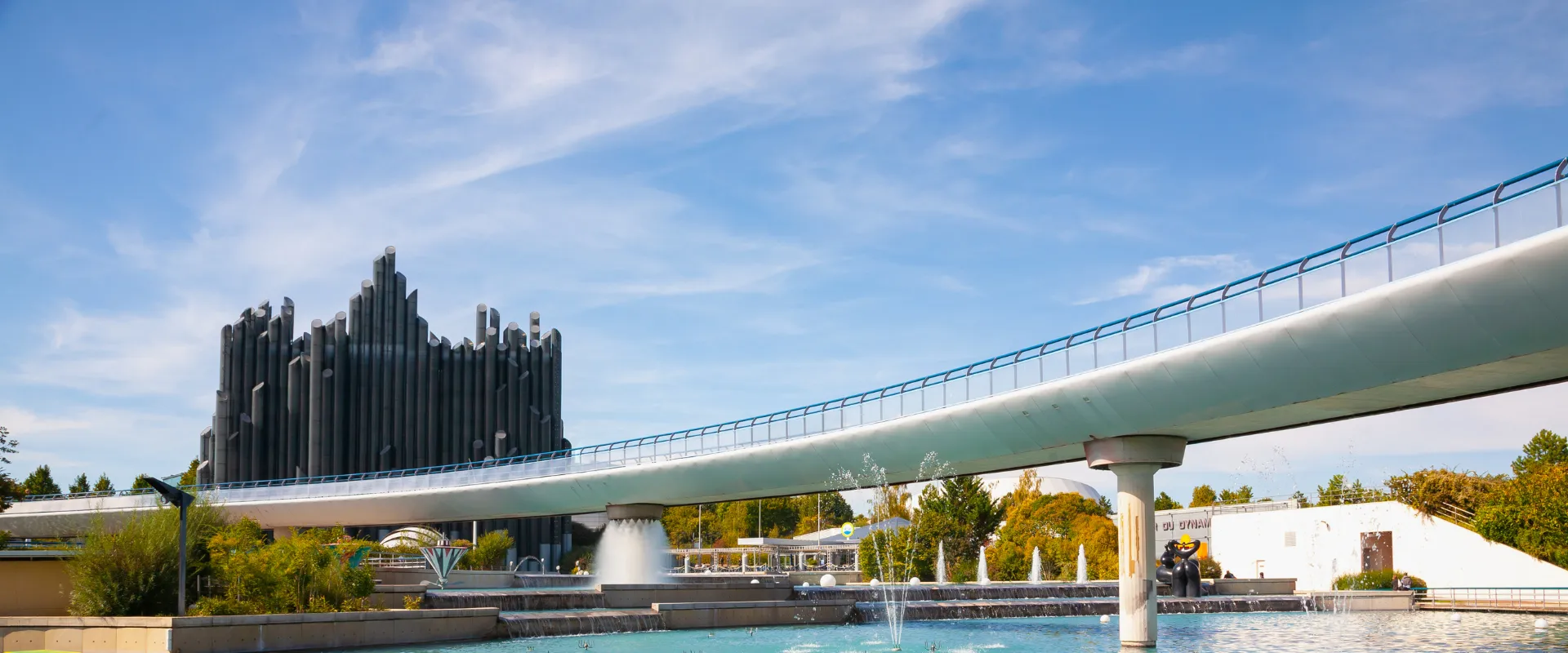 Pont moderne au-dessus d'un bassin avec sculpture noire architecturale et fontaines.