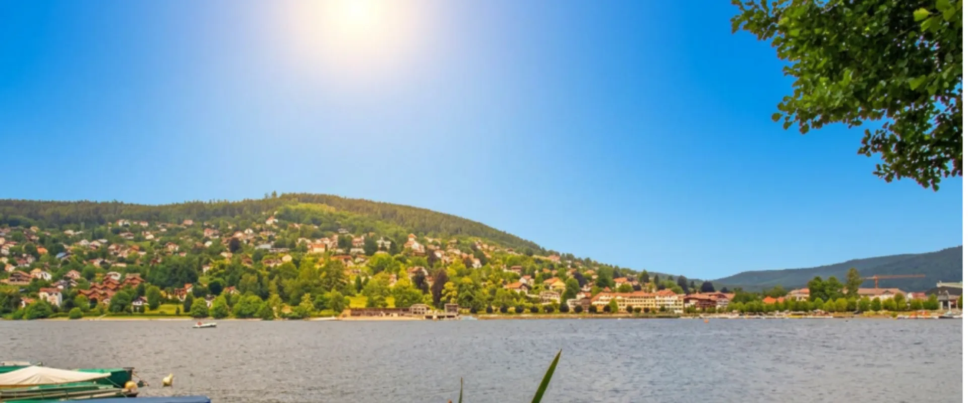 Lac de montagne avec village résidentiel, forêts vertes et maisons aux toits rouges.