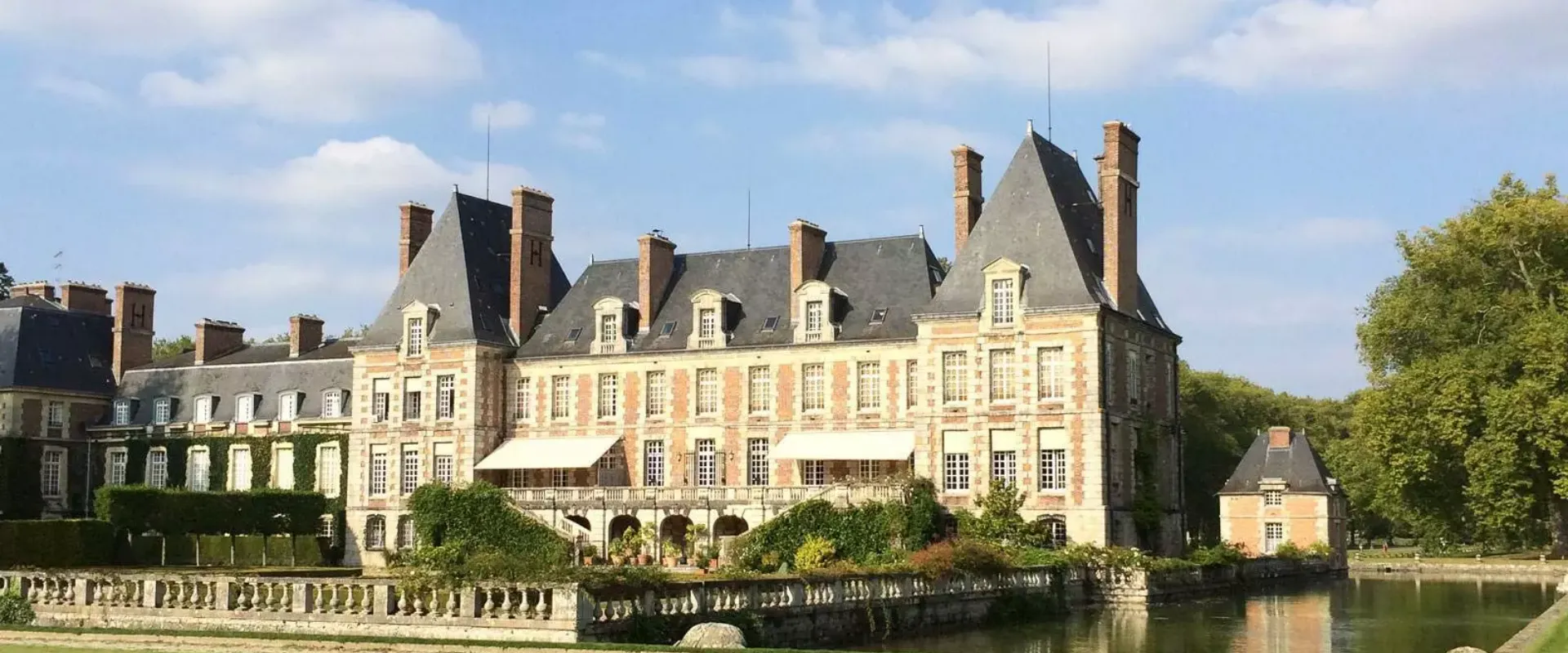 Château du XVIIe siècle en brique et pierre avec mansardes bordant rivière Essonne.