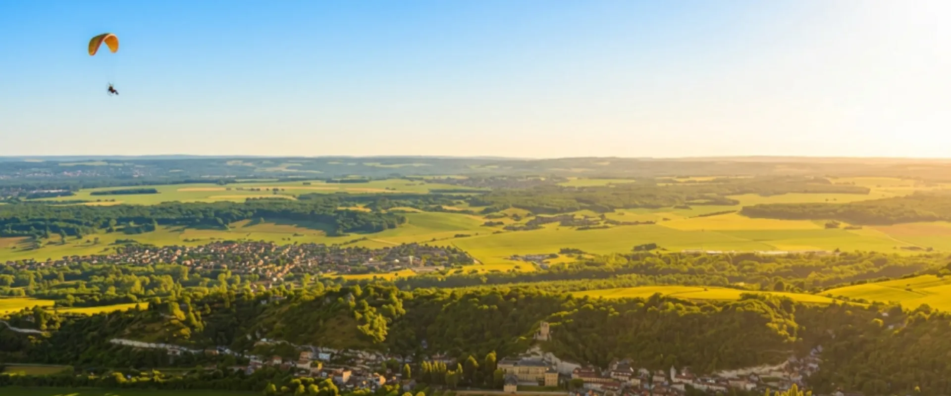 Vue aérienne vallée Val-d'Oise avec paraglutiste, champs verts et villages forestiers.